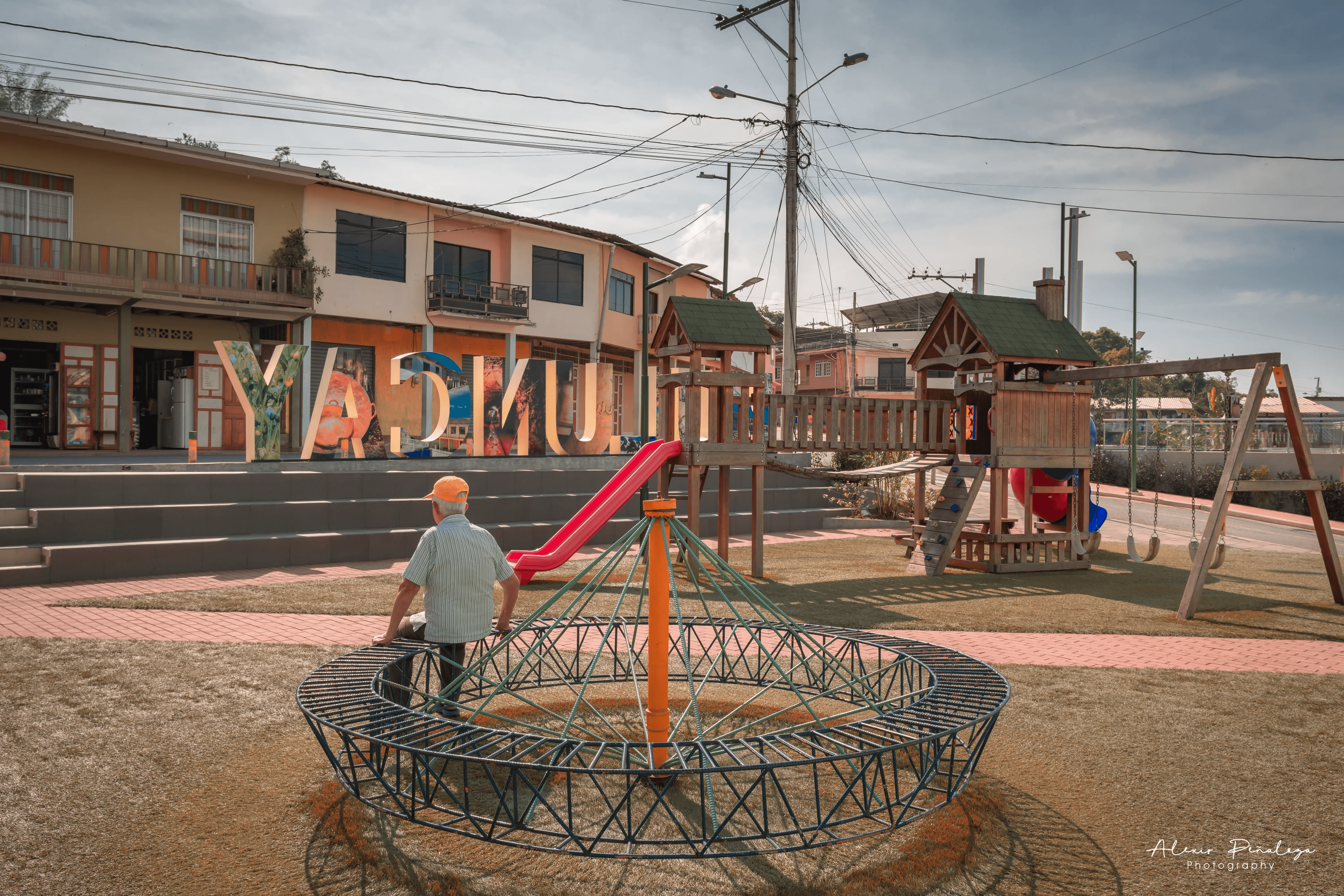 Hombre sentado en la estructura metálica del parque rodeado de juegos y letras turísticas