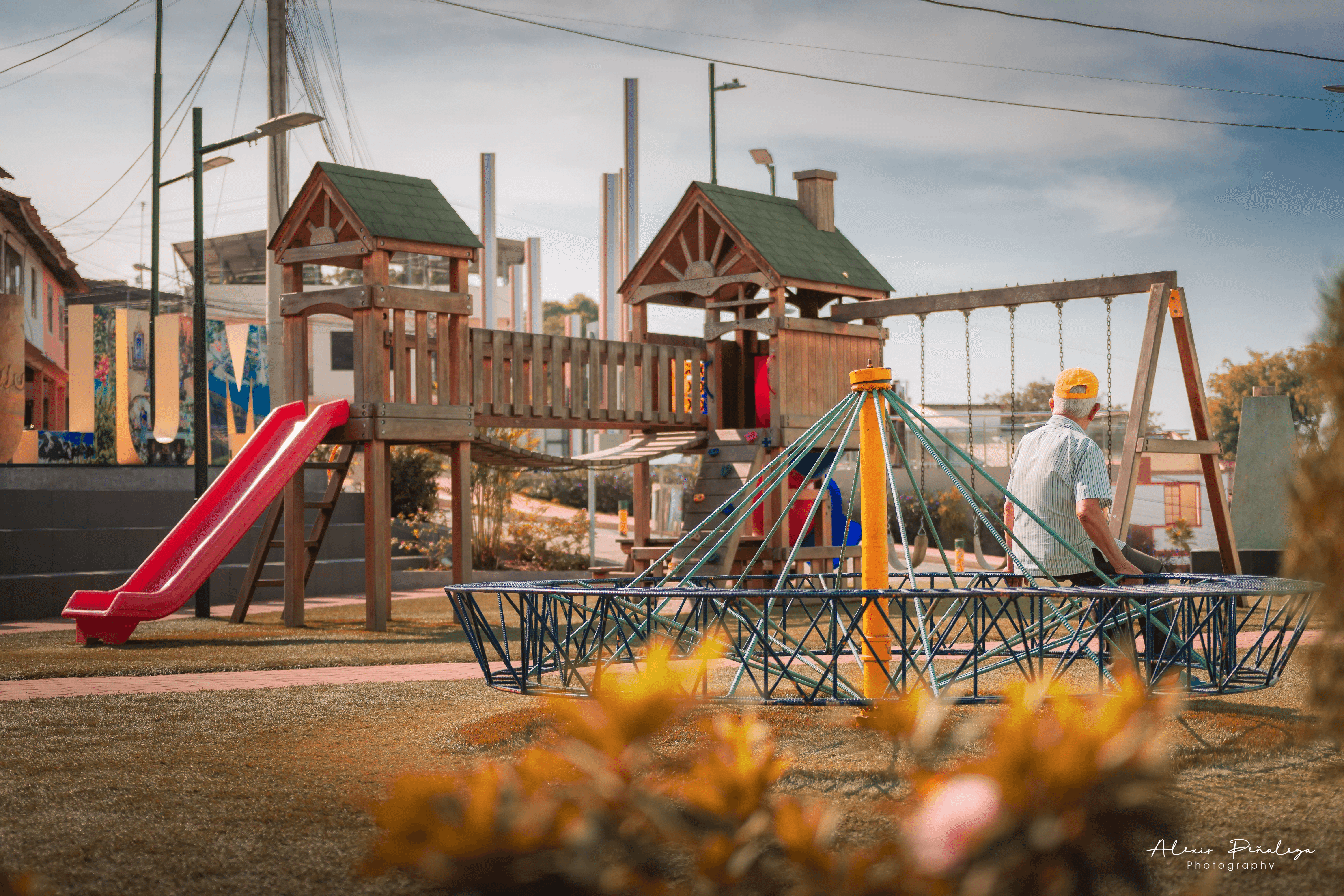 Señor con gorra amarilla sentado en un juego rodeado del área recreativa infantil