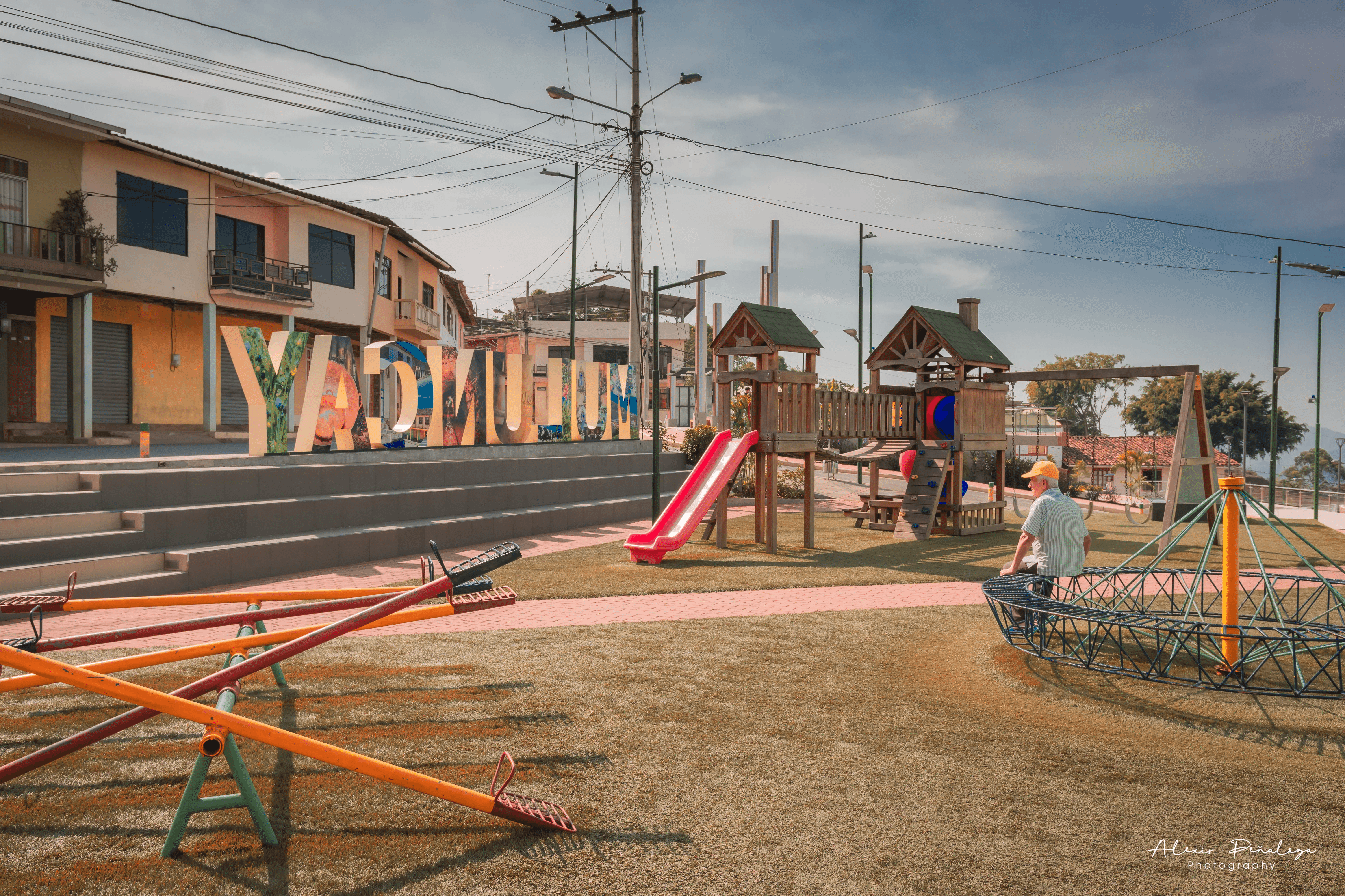 Sube y bajas del parque con un señor descansando y el letrero de Muluncay al fondo